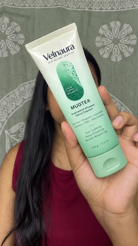 A woman holds a Mugtea tube close to the camera against a sage-gray curtain.