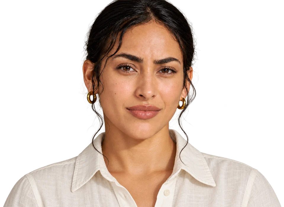 Head-and-shoulders portrait of a woman with dark, slicked-back hair and gold hoop earrings, raising one eyebrow with a sceptical, knowing look, in an ivory linen shirt.