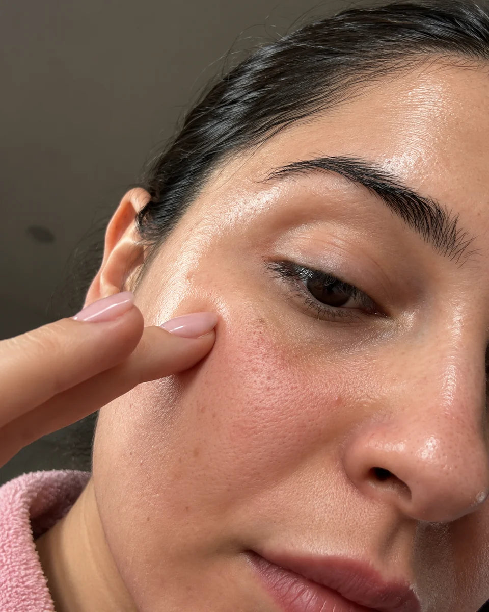 Close-up skincare selfie of a woman gently touching her cheek with her fingertips.