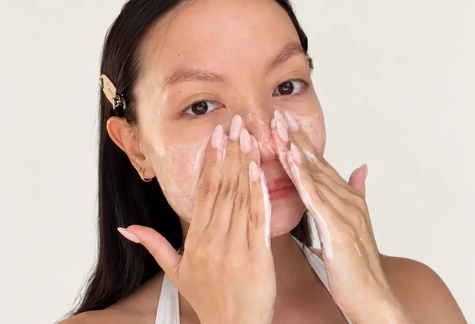 Woman gently massaging foamy cleanser around her nose and cheeks in soft, warm light.